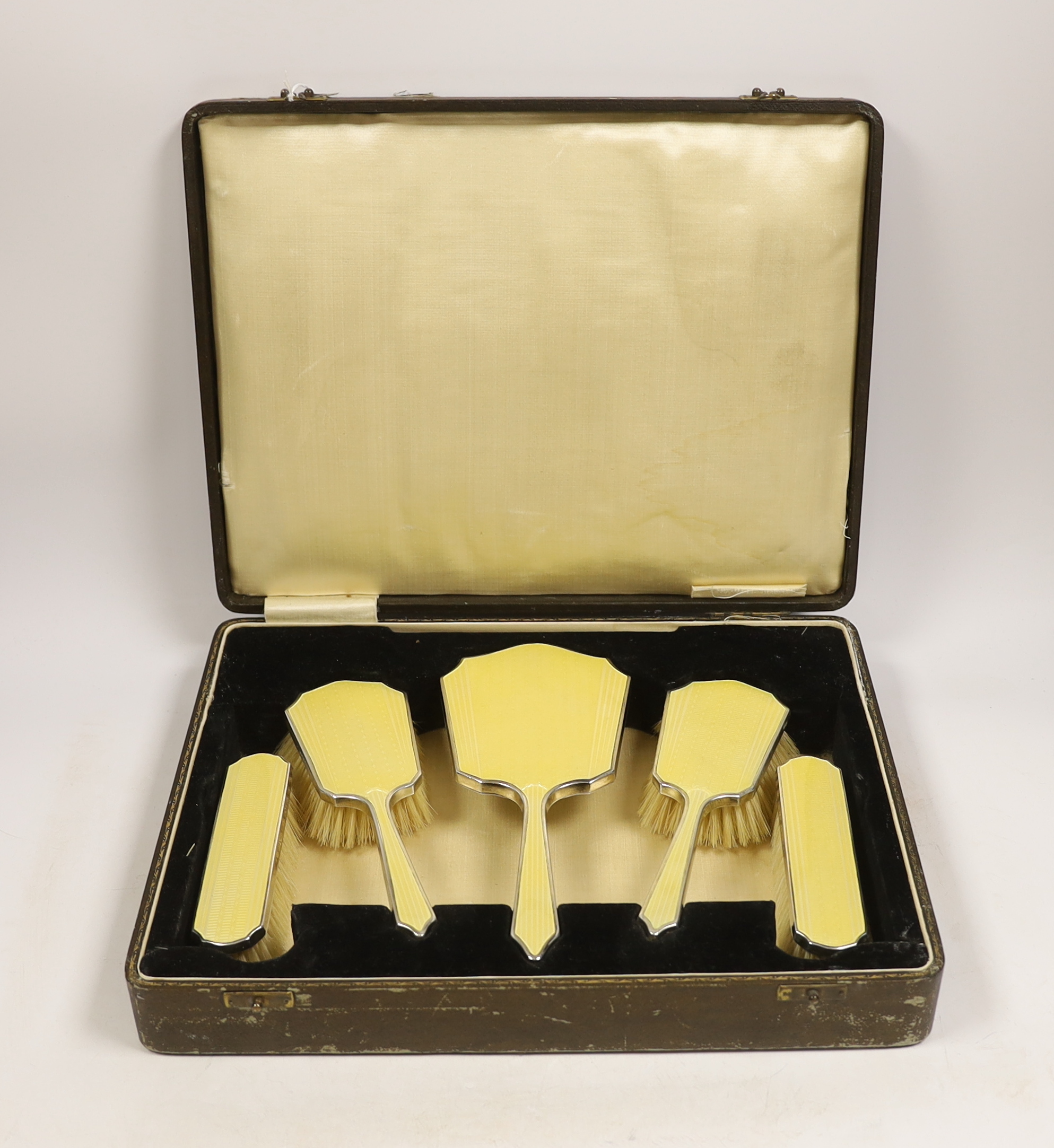 A cased George V silver and yellow guilloche enamel mounted five piece mirror and brush set, Hassett & Harper. Birmingham, 1935.